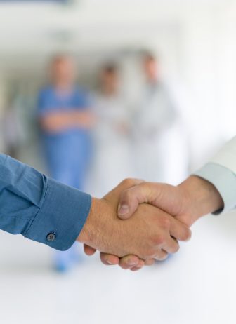 Close-up of a patient handshaking with a doctor at the hospital - healthcare and medicine concepts